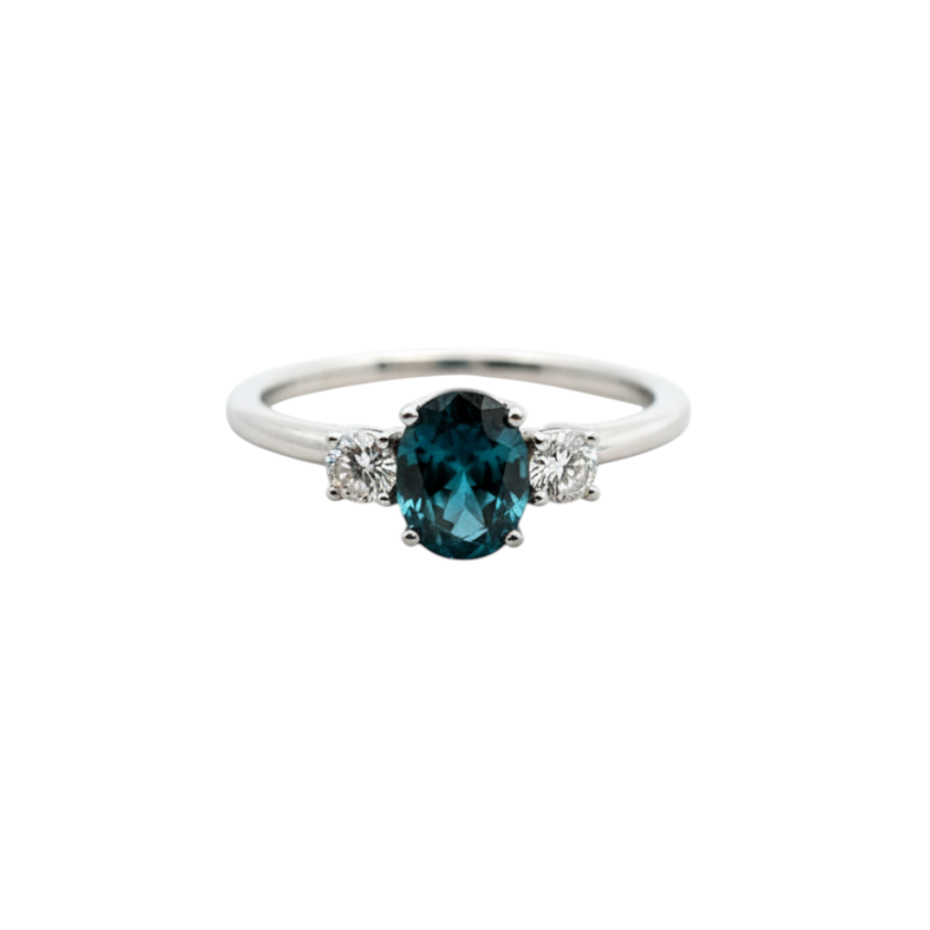 Caribbean Gems oval blue diamond ring with round side diamonds set in 14kt white gold on a white satin background.